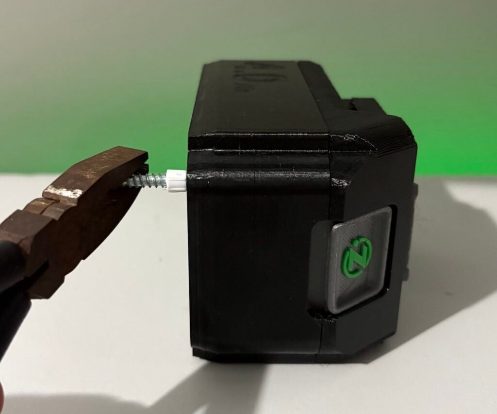 Removing the tamper-evident plastic screw plug from a Makita battery before fitting a custom battery button