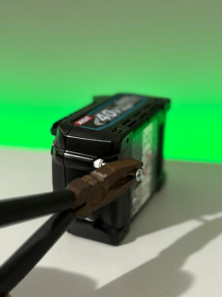 Removing the tamper-evident plastic screw plug from a Makita battery before fitting a custom battery button