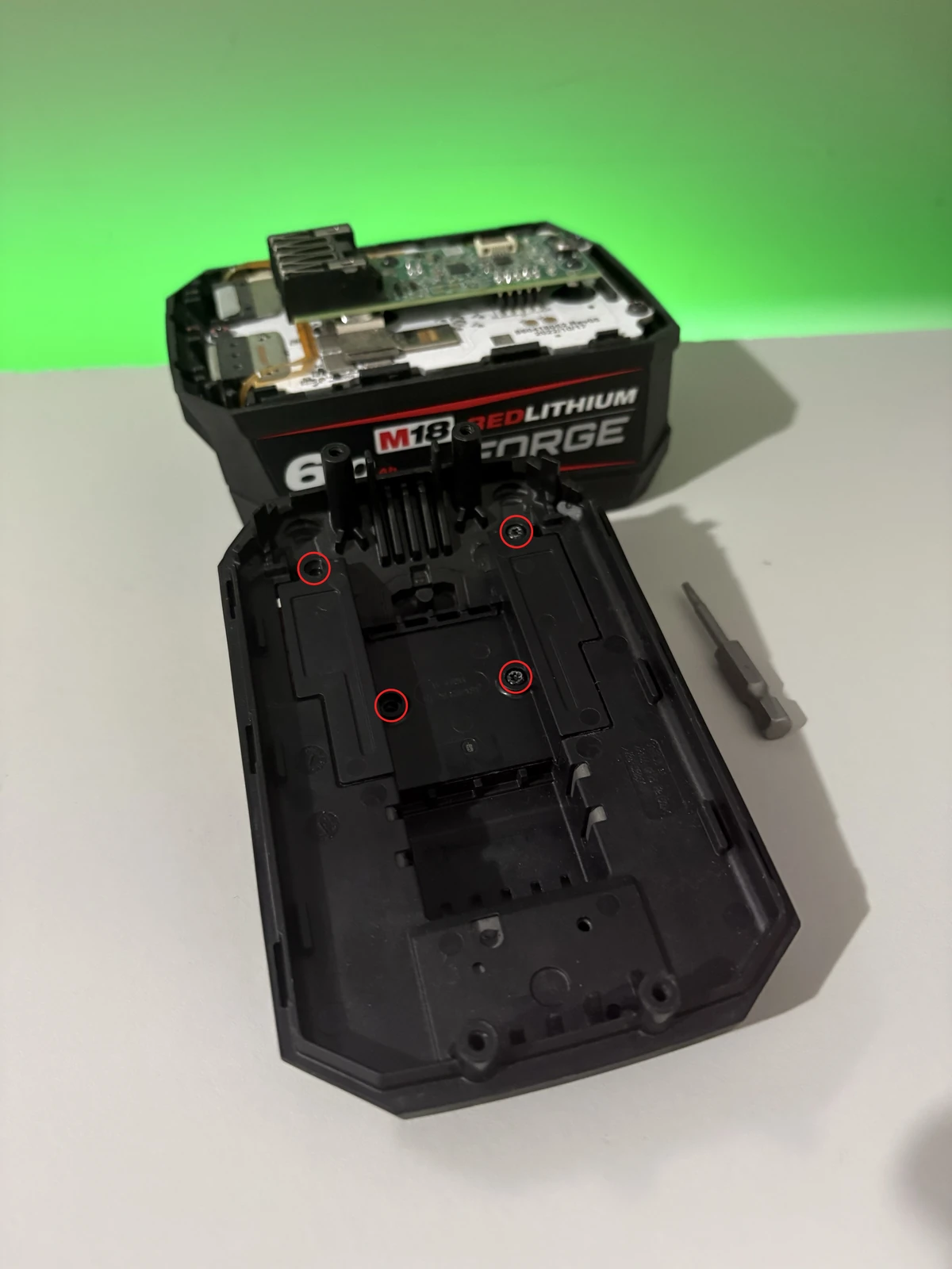 All four T8 retaining-plate screw positions circled in red inside the Milwaukee battery lid, with two screws already removed