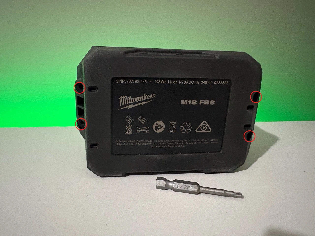 Four outer T10 screw holes circled in red on the underside of a Milwaukee M18 battery